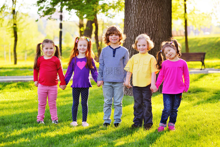 一群小孩子在草树和公园的背景上手牵微笑图片