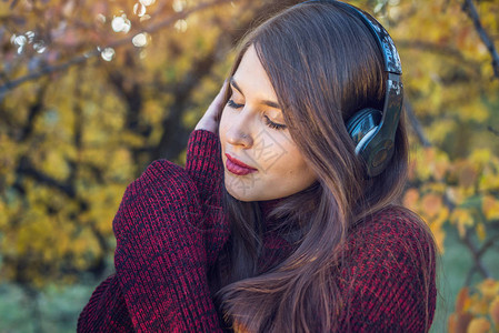 美丽的女人在秋天阳光公园站在大自然的背景下用耳机听音乐好心情最喜欢的音乐快背景图片