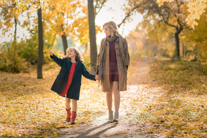 年轻漂亮的母亲和她的小女儿在秋天的背景下玩得开心图片