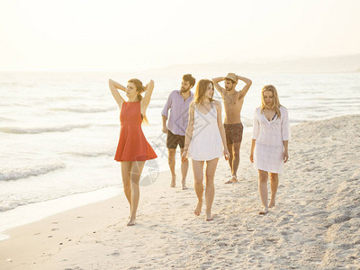 一群朋友在日落时沿着海滩散步图片