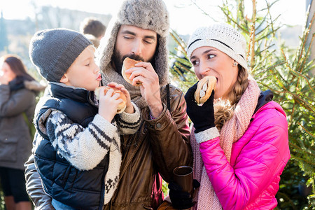一家人在树前的圣诞市场上吃面包卷和香肠图片
