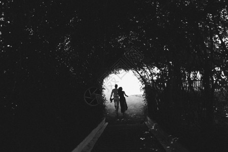 美丽的年轻夫妇穿过树木和灌木的隧道走图片