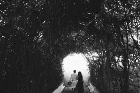 美丽的年轻夫妇穿过树木和灌木的隧道走图片