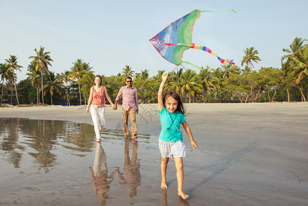 快乐的混血家庭在日落时分在海滩上玩耍父母与孩子玩耍孩子手里拿着风筝图片