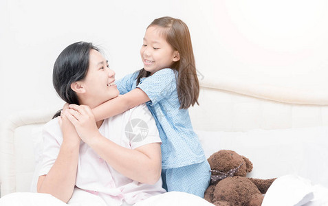 可爱的亚洲女孩微笑和拥抱妈在早上床图片