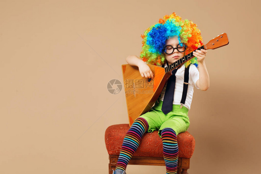 快乐的孩子们戴着大霓虹色假发弹巴拉莱卡的快乐小丑男孩戴着小丑假发和眼镜图片
