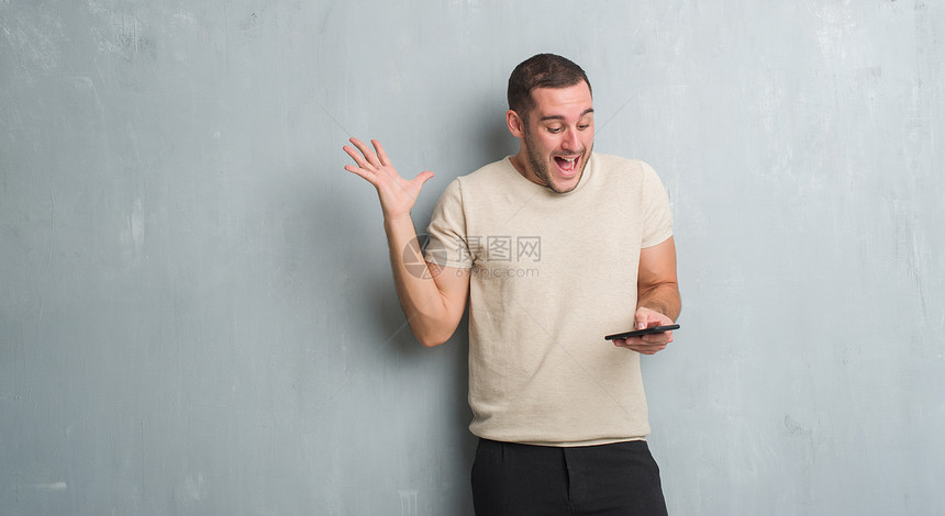 年轻的白人男子在灰色的格朗基墙上用智能手机发短信图片