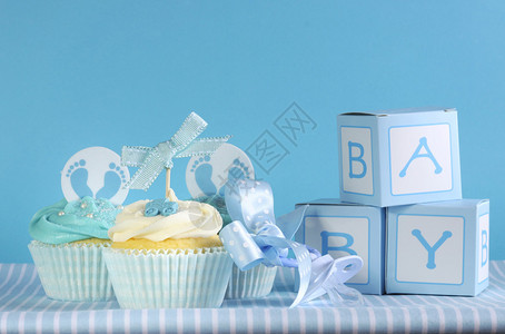 蓝色主题男婴三个纸杯蛋糕和婴儿喜欢蓝色背景的礼盒图片