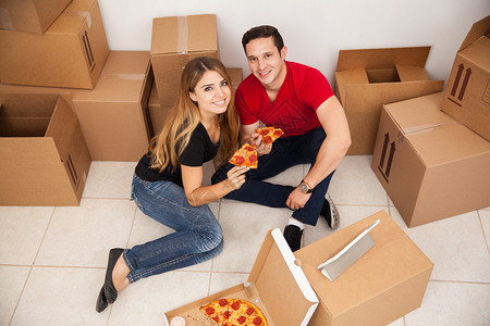 一对年轻夫妇在新家里拆开箱子一起吃披萨的高度图片