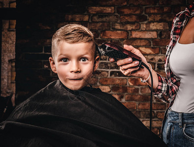 有趣的学龄前男孩理发带修剪器的儿童理发师正在带阁楼内部的房图片