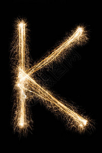 英文大字母K由黑色背景上的燃烧火花制成闪亮的节日烟花字体图片