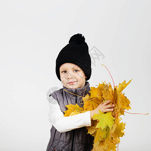 愉快的乐的美丽的小男孩画象反对白色背景的孩子拿着黄色的枫叶孩子吐出秋图片