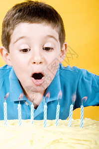 男孩在黄背景的蛋糕上吹蜡烛的图片