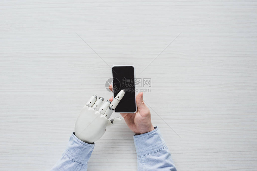 使用智能手机木制桌子上空白屏幕的半机械手男图片