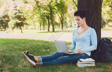 拥有笔记本电脑的短发女孩准备参加大学校园公草地上的考试图片