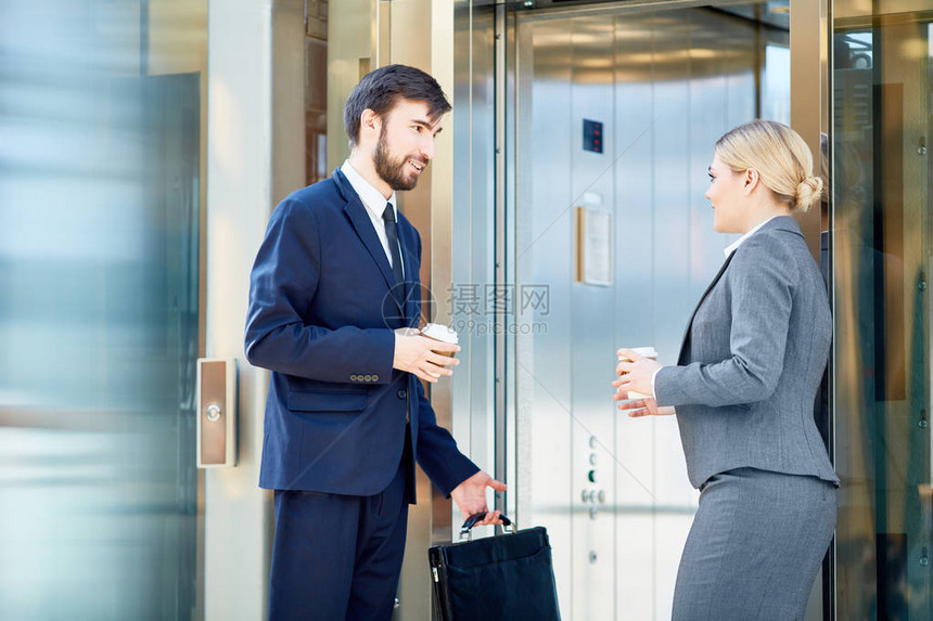 两名身着正式服装会议和乘电梯在上班途中通过电梯交谈的商业同事的肖像图片