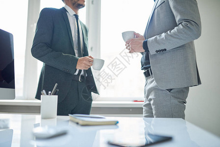 两位成功商人在现代办公室的咖啡休息时间端着杯子聊天图片