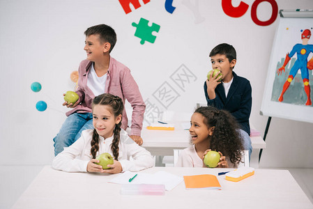 多民族儿童在课间休息时坐在教室里吃苹果图片