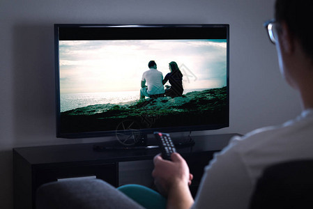 电视连续剧解读男人在家里用智能电视看电视或流媒体电影或连续剧电影或电视屏幕上的节目手持遥控器或切换频道的人打背景