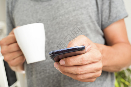一位身穿灰色T恤的年轻白人男子在室内使用智能手机图片
