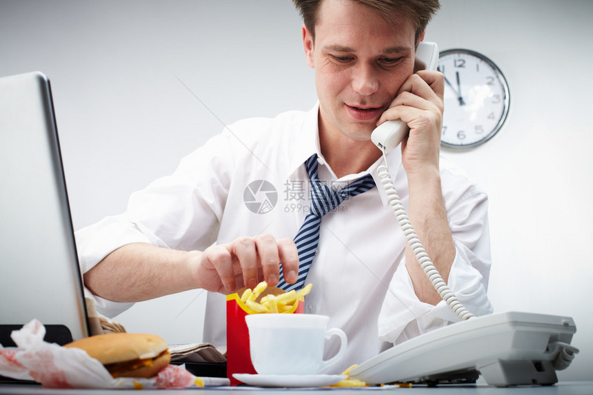 商务男士一边吃着薯条一边打电话沟通客户图片
