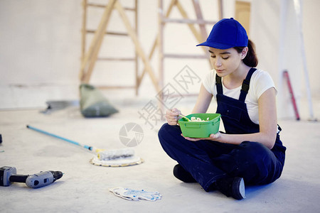 建筑工地午休时身穿工人制服的年轻女子盘腿坐在图片