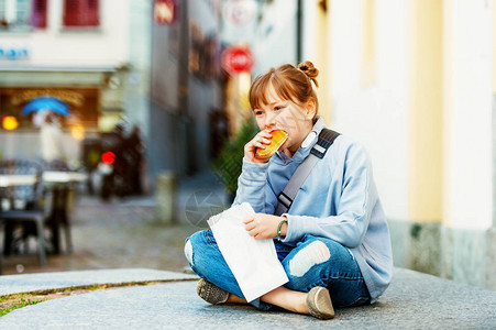 坐在街道旁吃面包的小女孩 图片
