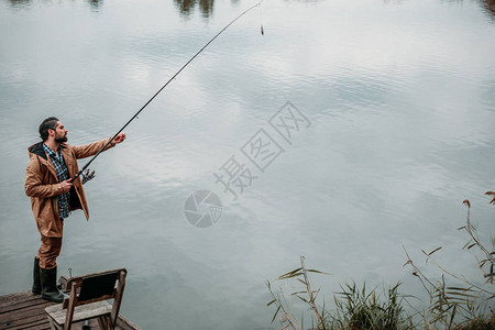 渔夫在湖边的木码头上用竿钓鱼图片