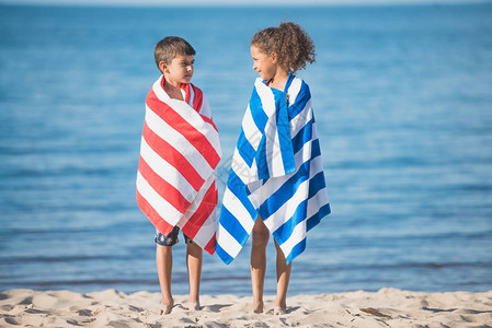 身穿毛巾的多文化儿童在海边站立时图片