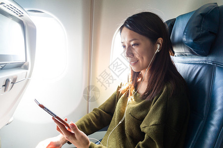 亚裔年轻女在飞机上听手机音乐的图片