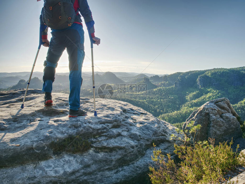 有固定腿的游客在前臂拐杖的帮助下踩到岩石山上图片