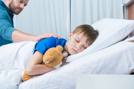 父亲抚摸着躺在医院病床上的生病的小儿子图片