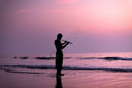 一名男子在日落时分的树枝上练习吹长笛图片