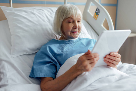 躺在床上和医院使用数字平板电脑的高级妇图片