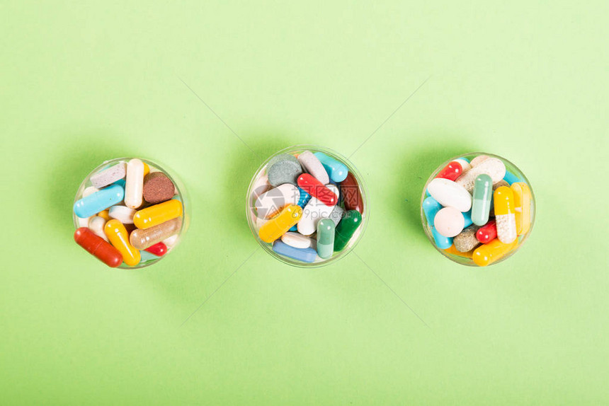 三杯五颜六色的药丸和绿色背景的药片图片