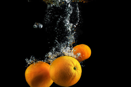 水中有气泡的橙子清洗水果黑色背景上的照图片