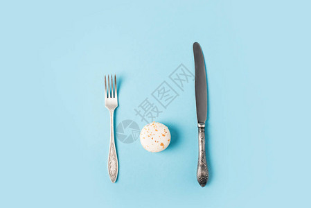 用蓝色隔开的甜马卡龙叉子和刀子的顶视图图片