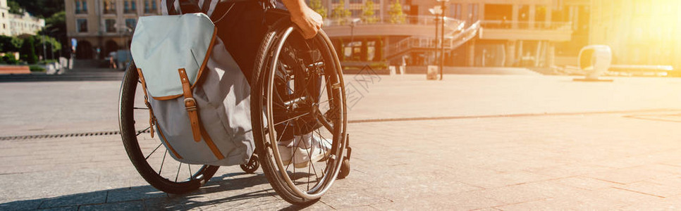 男子使用轮椅在街上用包袋和阳光背景图片