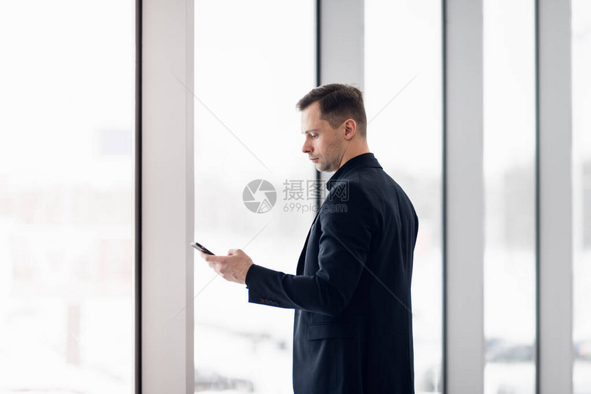 商人在机场使用手机应用程序年轻的商务专业人士在办公楼或机场航站楼内发短信给智能手机英俊的男人在室内穿着时图片