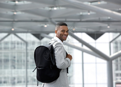 一个英俊年轻男子在机场微笑时带着袋子图片
