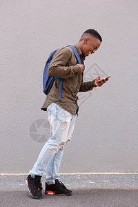 微笑的非洲男学生用手机和手提袋行走的图片
