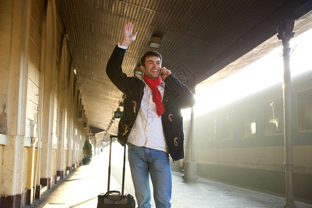 一名青年男子在火车站手挥和用手机图片