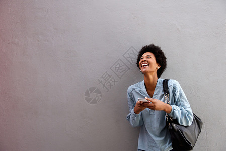 带着手机站在灰墙对面的非洲年轻女笑自喜的肖像图片