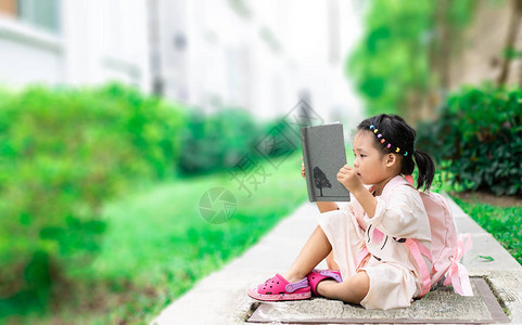 小女孩在读一本书背着包坐在公园里图片