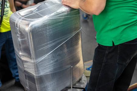 飞行前在机场出发航站楼用透明保护膜包裹手提箱的工人行李保图片