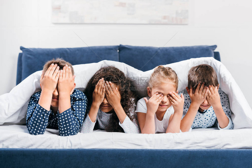 被蒙住眼睛的多文化儿童在家中用毯子躺在床上时遮着眼图片