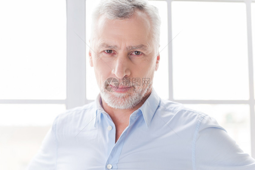 穿着衬衫自信的灰色头发上衣男子在站窗前看着摄像机时图片