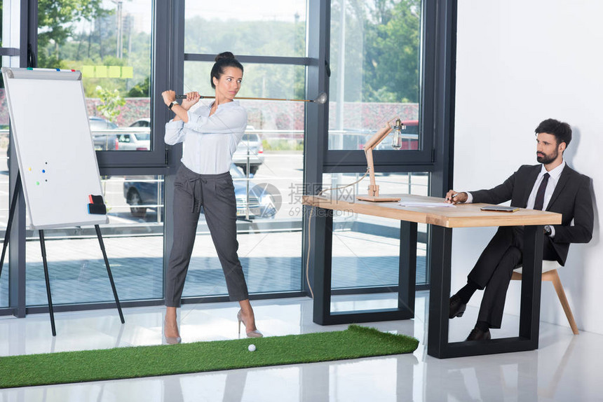 女商人打高尔夫球而同事坐在办公图片