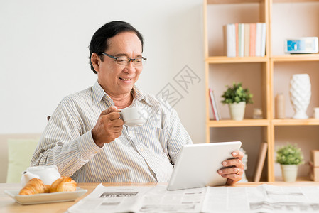 高年男子喝咖啡在数字平板电脑上而不是图片