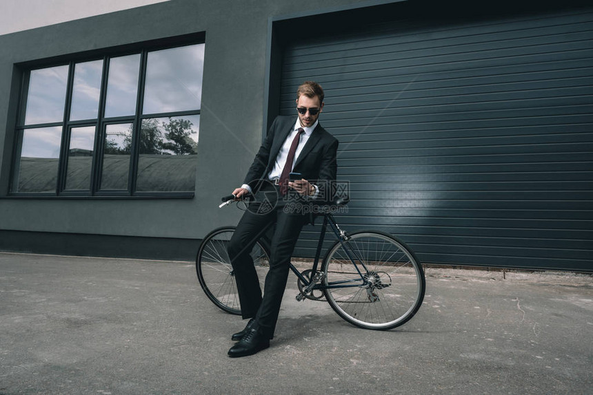 戴太阳眼镜坐在自行车上使用智能手机的年青图片